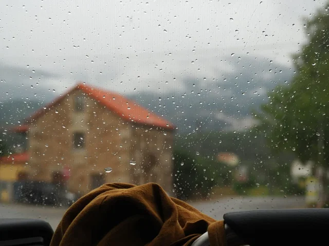 Casa vista através de uma janela molhada pela chuva durante uma tempestade, risco coberto pelo seguro multirriscos