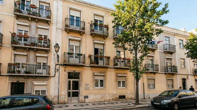 Fachada de prédio de apartamentos em Portugal com varandas de ferro, azulejos e entrada comum, numa rua com calçada portuguesa