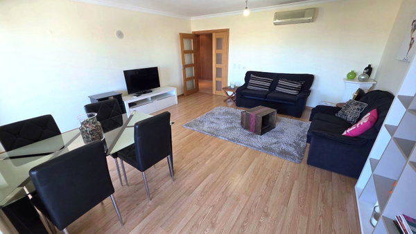 Sala com sofás pretos, mesa de jantar de vidro e chão laminado, apartamento T3 em Portimão